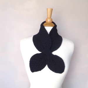 May include: A black knitted scarf shaped like a butterfly. The scarf is displayed on a white mannequin.
