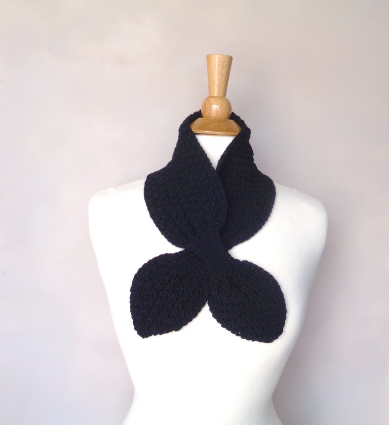 May include: A black knitted scarf shaped like a butterfly. The scarf is displayed on a white mannequin.