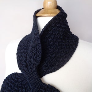 May include: A black knitted infinity scarf with a textured pattern. The scarf is draped over a white mannequin.