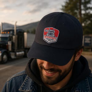 May include: Navy blue baseball cap with a red and white Interstate Trucking USA logo patch. The patch features a truck graphic and the number 26. The cap is made of a soft material.