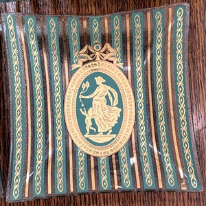 May include: Square glass dish with teal and gold vertical stripes. The center features an oval medallion with a teal image of a woman and child. The dish has a gold border and a decorative bow at the top.
