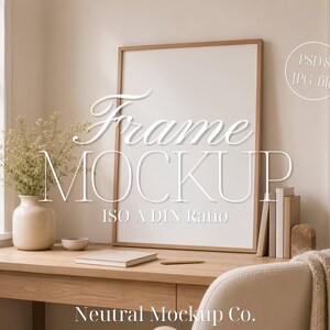 Puede incluir: Un marco de fotos vertical de madera clara con un centro blanco vacío, que presenta el texto Frame MOCKUP ISO A DIN Ratio y PSD & JPG file. El marco se apoya en un escritorio de madera junto a un jarrón beige con flores secas y libros.