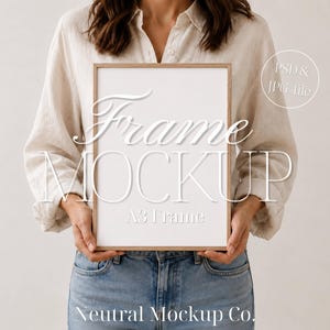 Op de afbeelding: Een A3-frame-mockup met een lichte houten afwerking en een wit interieur, vastgehouden door een persoon. De tekst "Frame Mockup" wordt weergegeven in een gestileerd lettertype. De woorden "PSD & JPG file" zijn ook zichtbaar. Het frame heeft een neutraal ontwerp.