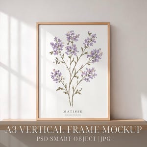 Pode incluir: Uma moldura de madeira vertical contendo uma impressão branca com uma ilustração em aguarela de flores roxas semelhantes a lavanda e caules verdes. A palavra MATISSE está impressa em letras maiúsculas pretas no centro inferior.