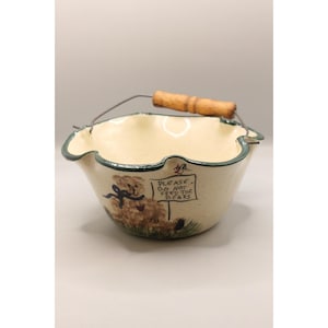 May include: Cream ceramic bowl with a green rim and a metal handle with a wooden grip. The bowl features a painted teddy bear and the text "PLEASE DO NOT FEED THE BEARS."