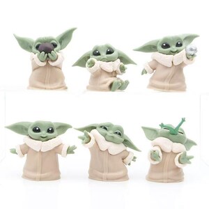 May include: A set of six small green figurines with large ears and black eyes, each wearing a tan robe with a white collar. The figures are posed in various actions, including holding a dark sphere, a silver ball, and eating a green plant.