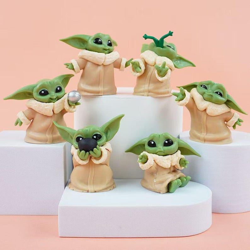 May include: A set of six small green alien figurines with large black eyes and pointed ears, each wearing a tan robe with a cream-colored collar. The figures are posed in various positions, with some holding small spherical objects or gesturing.