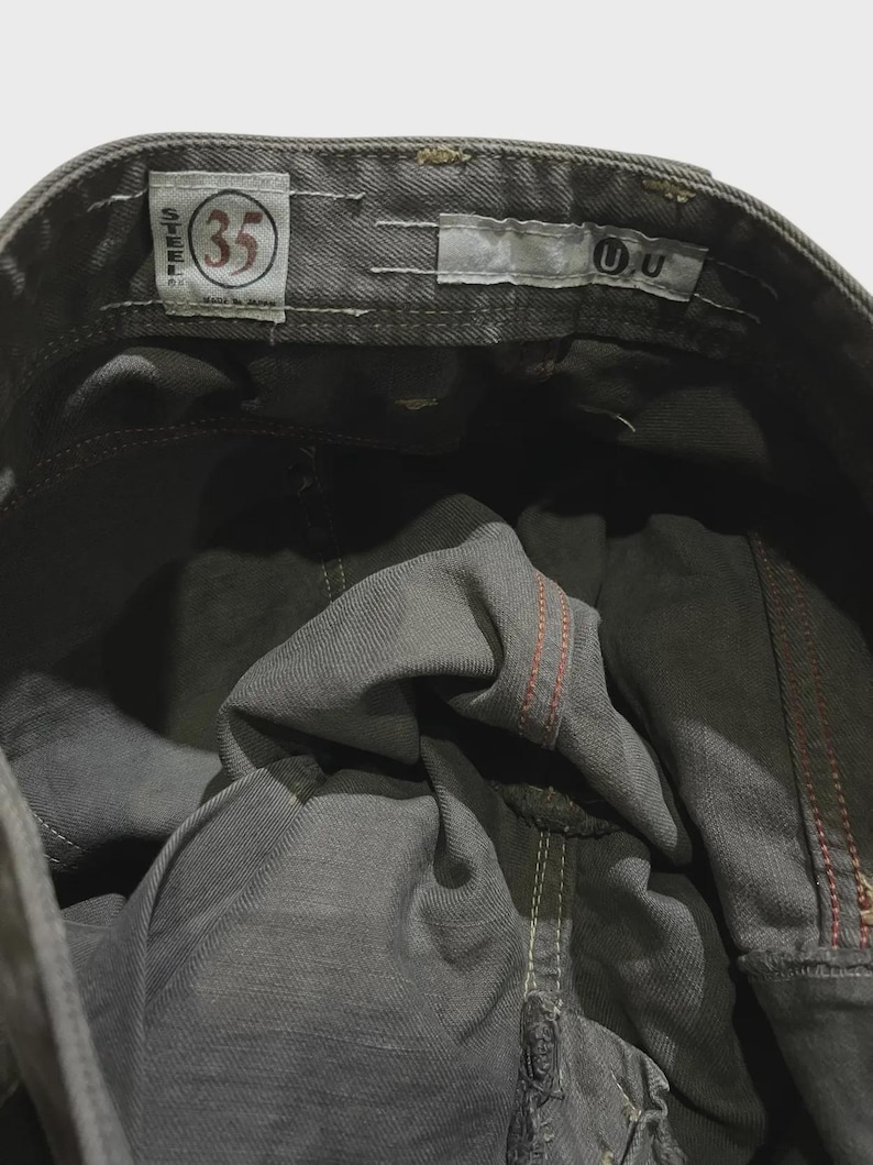 K&ouml;nnte beinhalten: Nahaufnahme der Innenseite einer grauen Jeans. Die Jeans hat ein Gr&ouml;&szlig;enetikett 35, und die N&auml;hte sind in Rot und Wei&szlig; sichtbar. Die Jeans wird in Japan hergestellt.