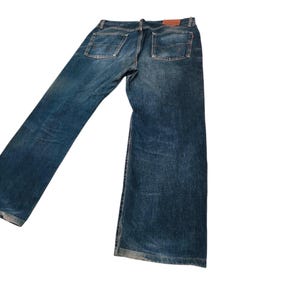 May include: Blue denim jeans with a classic five-pocket design. The jeans have a medium wash and a straight leg fit. A brown leather patch is visible on the back waistband. The jeans are made of durable denim.