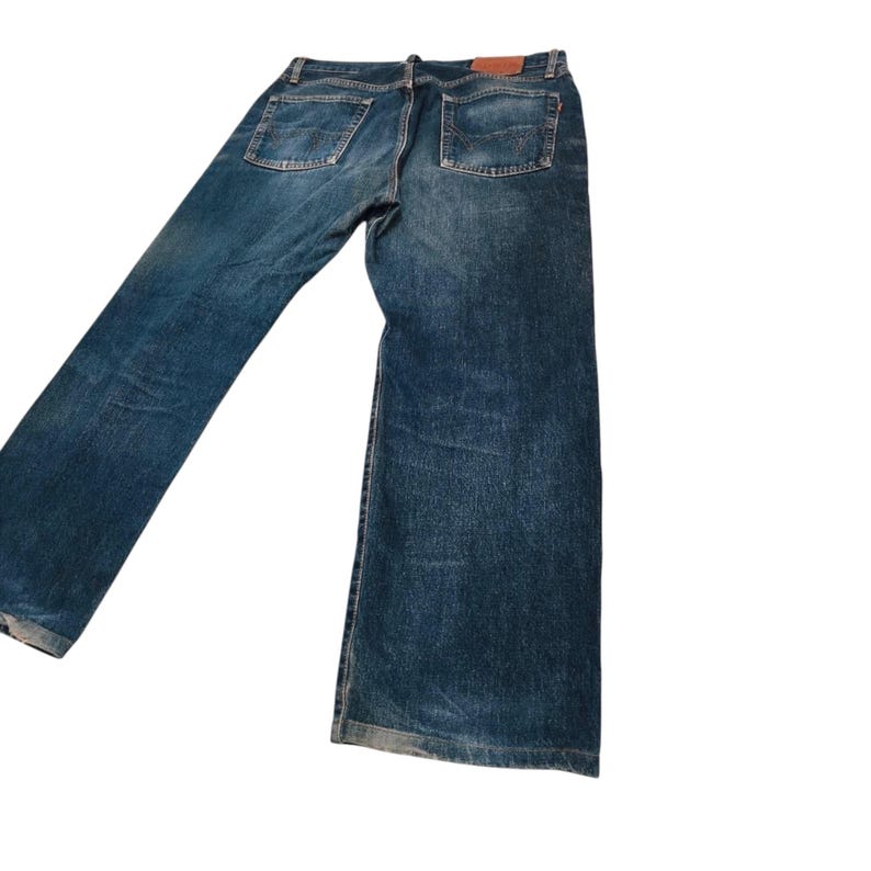 May include: Blue denim jeans with a classic five-pocket design. The jeans have a medium wash and a straight leg fit. A brown leather patch is visible on the back waistband. The jeans are made of durable denim.