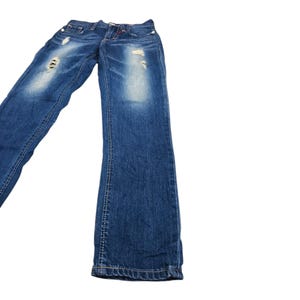 May include: Blue denim jeans with distressed details, including rips and faded patches. The jeans have a classic five-pocket design and a button and zipper closure. The stitching is visible in a contrasting color.