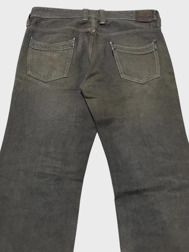 K&ouml;nnte beinhalten: Dunkel olivgr&uuml;ne Jeans mit zwei Ges&auml;&szlig;taschen und einem Lederaufn&auml;her. Die Jeans haben ein klassisches F&uuml;nf-Taschen-Design und eine gerade Beinpassform. Der Denim hat ein abgenutztes, verblasstes Aussehen.
