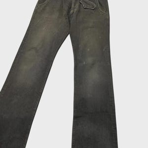 K&ouml;nnte beinhalten: Dunkelgraue Jeans aus Denim mit verwaschenem Aussehen. Die Jeans haben ein klassisches F&uuml;nf-Taschen-Design, einschlie&szlig;lich einer kleinen M&uuml;nztasche, sowie einen Knopf- und Rei&szlig;verschluss. Die Jeans sind leicht abgenutzt, mit subtilen Gebrauchsspuren.