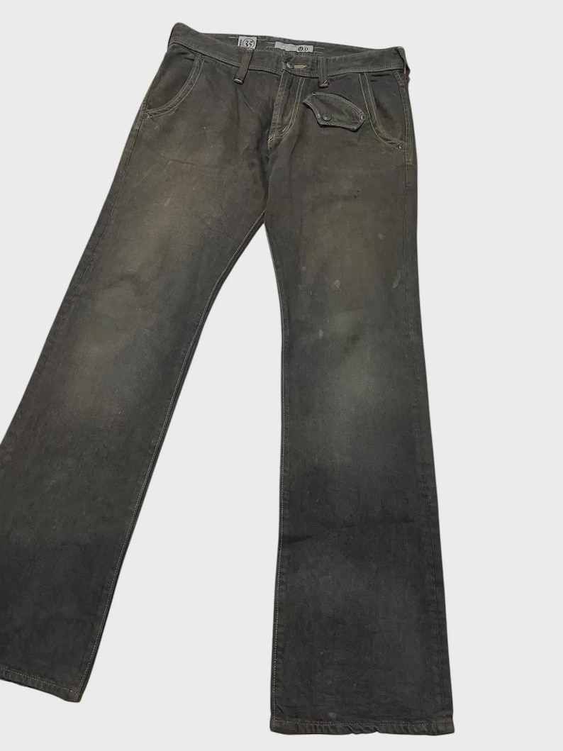 K&ouml;nnte beinhalten: Dunkelgraue Jeans aus Denim mit verwaschenem Aussehen. Die Jeans haben ein klassisches F&uuml;nf-Taschen-Design, einschlie&szlig;lich einer kleinen M&uuml;nztasche, sowie einen Knopf- und Rei&szlig;verschluss. Die Jeans sind leicht abgenutzt, mit subtilen Gebrauchsspuren.