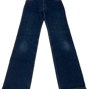 Puede incluir: Un par de pantalones vaqueros de mezclilla en tono oscuro con un diseño clásico de cinco bolsillos, cierre de botones y costuras visibles en color cobre. Los pantalones tienen un corte recto con un ligero desgaste en los muslos.