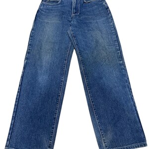 May include: A pair of medium-wash blue denim jeans featuring a classic five-pocket design, a button and zipper fly closure, and a straight-leg cut. The waistband includes belt loops and a small black brand label centered at the back.