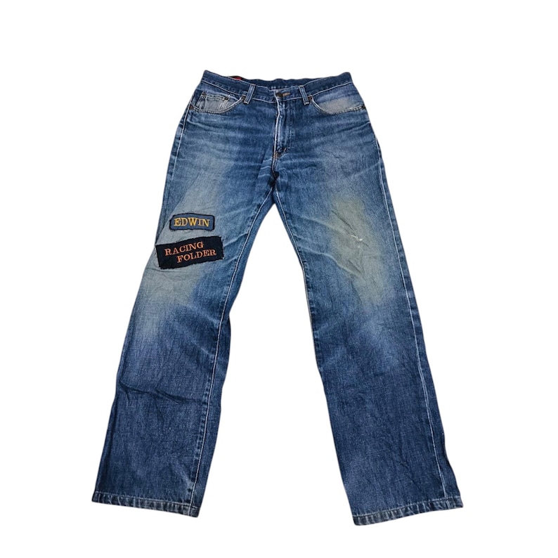 Puede incluir: Vaqueros azules descoloridos con corte recto. Los vaqueros tienen dos parches en la pierna izquierda con el texto "EDWIN" y "RACING FOLDER". Dise&ntilde;o cl&aacute;sico de cinco bolsillos. Aspecto vintage.