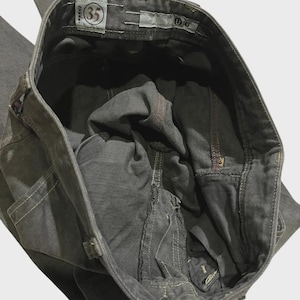 K&ouml;nnte beinhalten: Nahaufnahme einer grauen Jeans. Die Jeans hat einen Knopfverschluss und einen Rei&szlig;verschluss. Das Gr&ouml;&szlig;enetikett lautet "35". Die N&auml;hte sind in wei&szlig;em und rotem Faden sichtbar. Die Jeans ist gefaltet und zeigt die Innentaschen und den Bund.