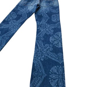 May include: Blue denim jeans with a light blue paisley pattern. The jeans have a classic five-pocket design and a straight leg. The back pockets and waistband are visible.