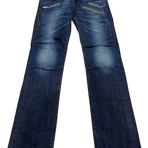 May include: Dark blue denim jeans featuring a faded wash, a button and zipper fly closure, and multiple silver-toned metal zipper pockets on the front. The pants have a straight-leg cut with visible stitching details and a structured waistband.