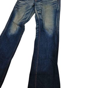 May include: Blue denim jeans with a faded wash and flared leg. The jeans have a classic five-pocket design, a button and zipper closure, and visible stitching. The denim has a worn appearance.