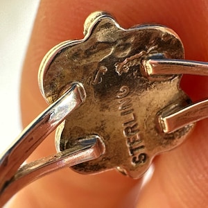 May include: Close-up of a sterling silver ring with a floral design. The ring's underside is stamped with the word "STERLING". The ring has a delicate, vintage aesthetic.