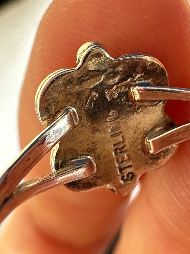 May include: Close-up of a sterling silver ring with a floral design. The ring's underside is stamped with the word "STERLING". The ring has a delicate, vintage aesthetic.