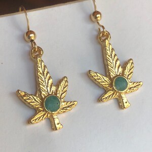 Könnte beinhalten: Goldene Marihuana-Blatt-Ohrringe mit grünen Stein-Akzenten.