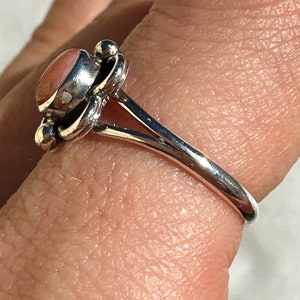 May include: A silver ring featuring a pink oval gemstone. The ring has a floral design around the stone and a smooth, polished band. The ring is shown on a finger.