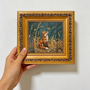 May include: A square framed painting featuring a red fox sitting in a field of tall grass and wildflowers, looking up at a small orange butterfly. The artwork is enclosed in an ornate, metallic gold frame with intricate decorative carvings.
