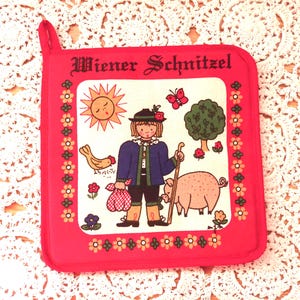 May include: A square red potholder featuring the text Wiener Schnitzel at the top. The center illustration depicts a person in a blue jacket and hat holding a walking stick and a red checkered bag, accompanied by a pig, a chicken, a sun, and a tree.