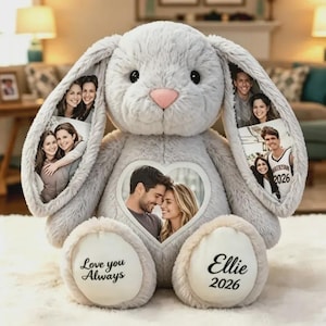 Puede incluir: Un peluche de conejo gris con un marco de fotos en forma de corazón en el pecho, fotos impresas en sus largas orejas y plantas de los pies blancas. La planta izquierda dice Love you Always y la derecha Ellie 2026 en texto negro.