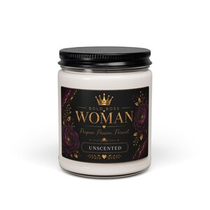 Puede incluir: Una vela blanca en un frasco de vidrio transparente con tapa negra. La etiqueta es negra con texto dorado que dice BOLD BOSS WOMAN, Purpose, Passion, Pursuit y UNSCENTED, con detalles de corona y flores doradas a los lados del texto.