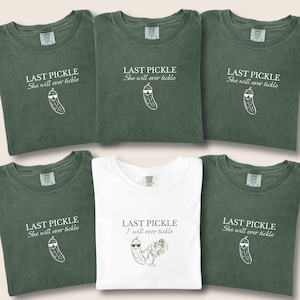 May include: Six t-shirts are shown, with a mix of olive green and white. Each has the text "LAST PICKLE" and "She will ever tickle" or "I will ever tickle" along with a cartoon pickle wearing sunglasses. The shirts are neatly folded.
