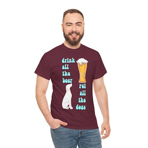 Puede incluir: Camiseta granate con el texto "drink all the beer pet all the dogs" en azul claro. La camiseta presenta una imagen de dibujos animados de un vaso de cerveza y un perro.