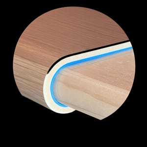 May include: Close-up of a wooden table corner with a curved edge. The table has a light brown wood grain finish, a white border, and a thin blue accent line. The design is modern and minimalist.