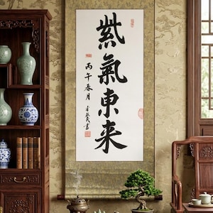 Puede incluir: Escena interior de inspiración asiática con un pergamino de caligrafía con caracteres negros. Un mueble de madera exhibe jarrones y libros. Una pequeña mesa sostiene un bonsái y un quemador de incienso, con una silla de madera cerca.