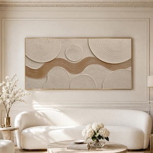 Peut inclure: Une grande œuvre d'art murale rectangulaire présentant une composition abstraite et texturée de formes circulaires beiges et fauves, reliées par un motif central en vague horizontale, le tout encadré d'un fin bord doré métallique.