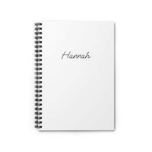 Op de afbeelding: Een wit spiraalgebonden notitieboek met de naam "Hannah" in cursief geschreven. Het notitieboek heeft een strak, minimalistisch ontwerp, ideaal voor notities of journaling. De spiraalbinding is zwart.