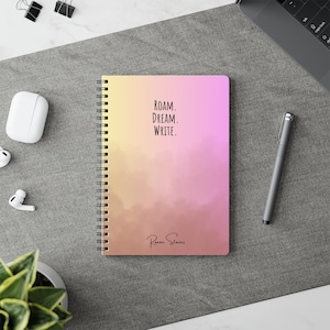 Op de afbeelding: Een spiraalgebonden notitieboek met een omslag die overloopt van geel naar roze. De omslag heeft de tekst "ROAM. DREAM. WRITE." in zwart, met "Peoni Stories" eronder. Een pen en andere kantoorbenodigdheden zijn zichtbaar.