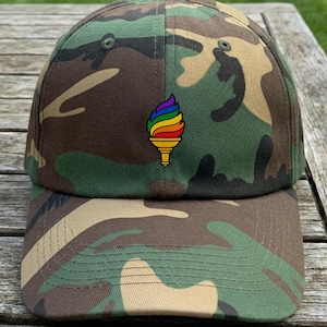 May include: A camouflage baseball cap with a rainbow ice cream cone design. The cap features a curved brim and a button on top. The hat is green, brown, and tan.