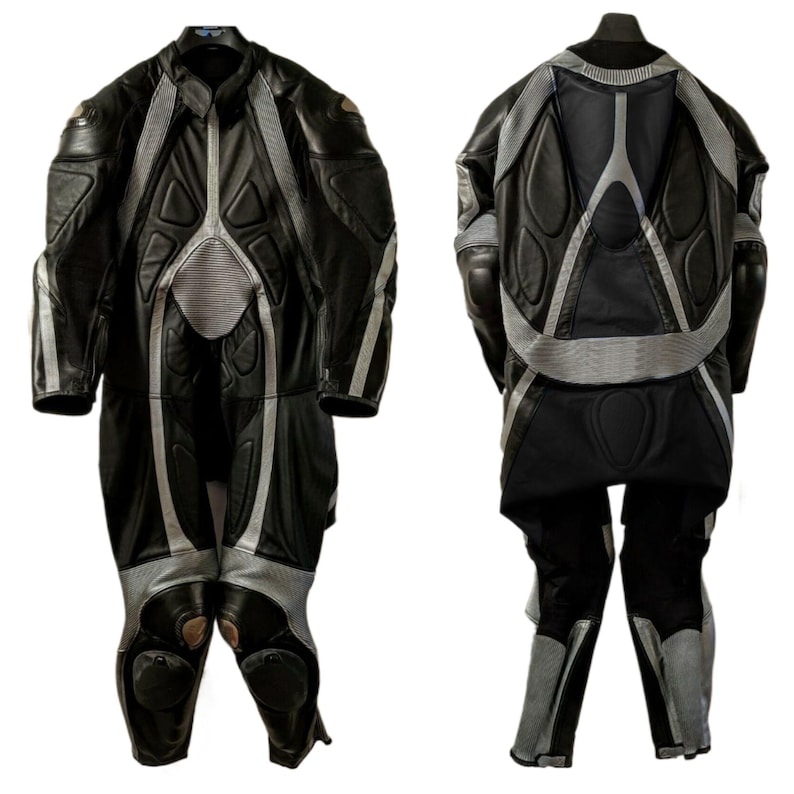 May include: Black and gray motorcycle racing suit. The suit is made of leather and features padded sections on the shoulders, elbows, chest, and knees. Silver stripes run along the sides and back of the suit.
