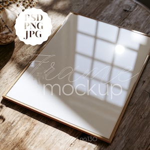May include: A rectangular picture frame with a thin metallic gold border and a reflective glass surface. The frame displays a white background with the text PSD PNG JPG in a scalloped circle and the words Frame mockup in cursive script.