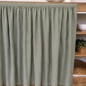 Op de afbeelding: Een saliegroen stoffen gordijn met een geplooide bovenkant, ontworpen om een open kast te bedekken. Het gordijn hangt in verticale plooien en biedt een solide, ondoorzichtige afdekking voor de opbergruimte met een strak en eenvoudig uiterlijk.