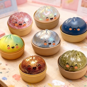 May include: Seven colourful, smiling dumpling-shaped containers are displayed. Each dumpling has a different colour and texture, including pink glitter, pearlescent white, blue, yellow-green, silver, brown glitter, and green with gold flecks. The containers are in light brown bowls.
