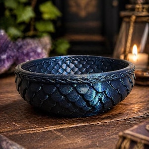Puede incluir: Un cuenco azul oscuro con una textura similar a escamas, que recuerda a las escamas de dragón. El cuenco tiene un borde texturizado y está sobre una superficie de madera. Es un objeto decorativo.
