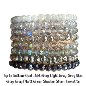 Peut inclure: Une pile de huit bracelets de perles en cristal &agrave; facettes dispos&eacute;es en d&eacute;grad&eacute; de couleurs. Le texte ci-dessous indique : Top to Bottom: Opal Light Gray, Light Gray, Gray Blue, Gray, Gray Multi, Green Shadow, Silver, Hematite.