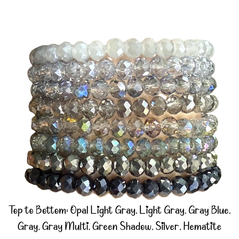 Peut inclure: Une pile de huit bracelets de perles en cristal &agrave; facettes dispos&eacute;es en d&eacute;grad&eacute; de couleurs. Le texte ci-dessous indique : Top to Bottom: Opal Light Gray, Light Gray, Gray Blue, Gray, Gray Multi, Green Shadow, Silver, Hematite.