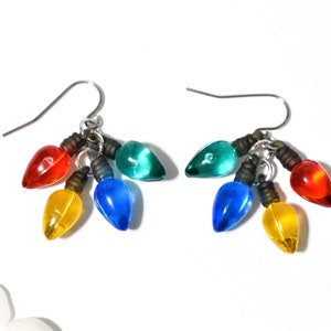 May include: A pair of dangle earrings featuring clusters of miniature, translucent, multi-colored light bulb charms in red, yellow, blue, and green. Each charm has a dark base and is attached to a silver-toned metal hook for pierced ears.