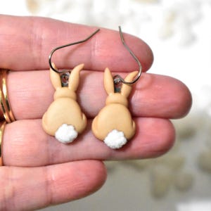 May include: A pair of dangle earrings featuring a brown bunny rabbit with a white fluffy tail. The earrings are made of polymer clay and have silver hooks.